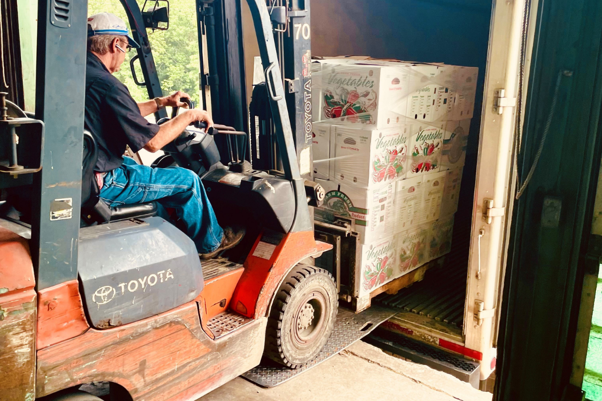 man driving forklift loading boxes of vegetables onto a semi-truck